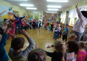 Dzieci tańczą w kole z rękoma uniesionymi w górę.